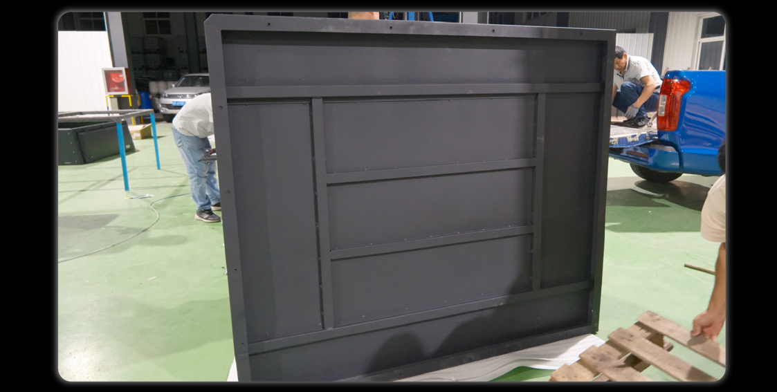 Dark grey base cover panel being assembled in factory workshop with workers