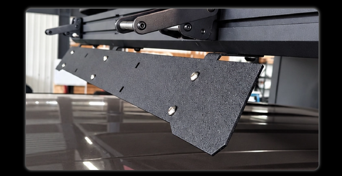 Close-up of wind deflector plate with stainless steel bolts and powder-coated black texture mounted on camper rail